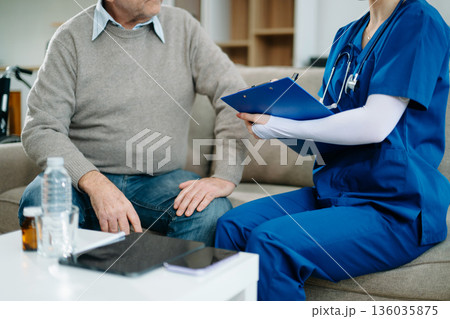 Senior man with chest pain speaks to nurse noting symptoms on tablet at home. Healthcare, heart health 136035875