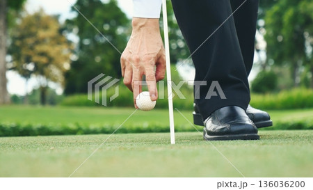 Businessman playing Golf ball practice hit swing on tee in golf club outdoor green field with recreation sport training course. Business men with black Suit driving golf Hobbies 136036200