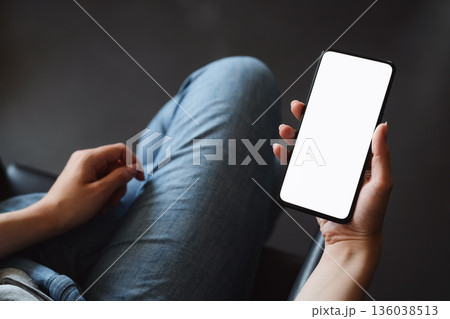Young woman hold smarphone with white screen while sitting in a chair Young woman hold smarphone with white screen while sitting in a chair 136038513