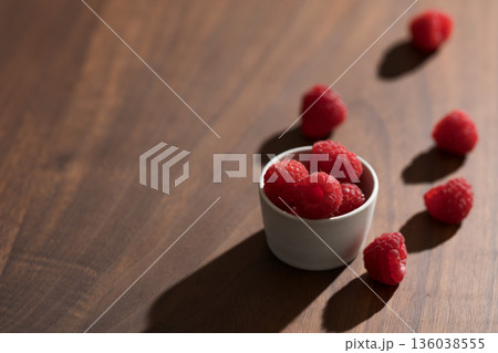 Fresh raspberries in small white bowl on wood table closeup Fresh raspberries in small white bowl on wood table closeup 136038555
