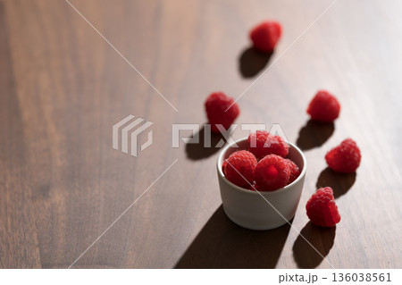 Fresh raspberries in small white bowl on wood table closeup Fresh raspberries in small white bowl on wood table closeup 136038561