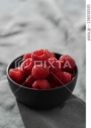 Raspberries in black bowl on linen napkin closeup Raspberries in black bowl on linen napkin closeup 136038585