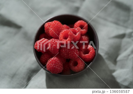 Raspberries in black bowl on linen napkin closeup Raspberries in black bowl on linen napkin closeup 136038587