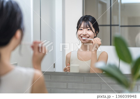 洗面所で鏡を見ながら歯磨きをする若いアジア人女性 洗面所で鏡を見ながら歯磨きをする若いアジア人女性 136039948