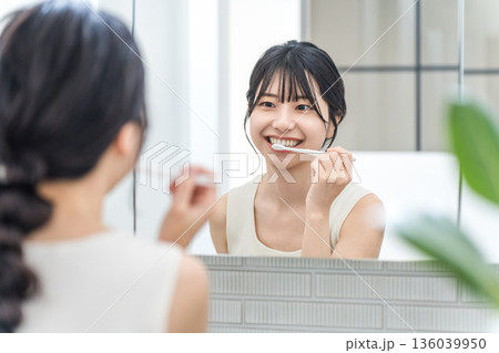洗面所で鏡を見ながら歯磨きをする若いアジア人女性 洗面所で鏡を見ながら歯磨きをする若いアジア人女性 136039950