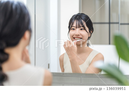 洗面所で鏡を見ながら歯磨きをする若いアジア人女性 洗面所で鏡を見ながら歯磨きをする若いアジア人女性 136039951