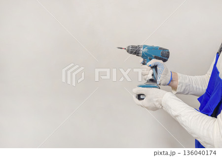 A person is holding a power drill with gloves on 136040174