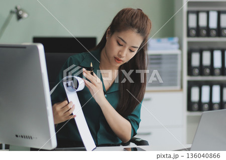 Determined asian businesswoman works late in a modern office, confidently analyzing data on her laptop, embodying success and professionalism with a smile Determined asian businesswoman works late in a modern office, confidently analyzing data on her laptop, embodying success and professionalism with a smile 136040866