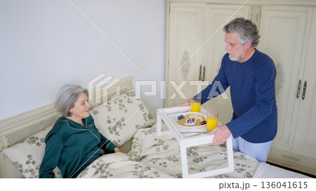 Husband bringing breakfast in bed to wife showing loving care Husband bringing breakfast in bed to wife showing loving care 136041615