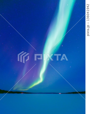 Panoramic horizontal view of the aurora borealis dancing over a frozen lake in Scandinavia. 136041942