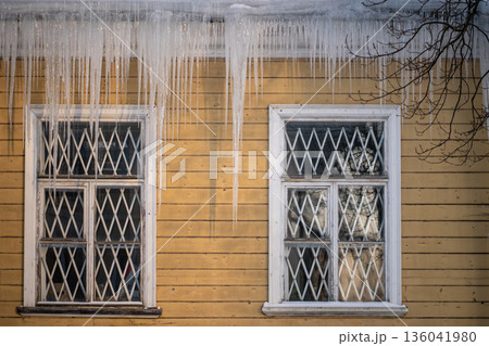 Icicles hang outside from roof at house, dangerous iced formations, winter problem for living areas. 136041980