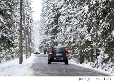 Car driving on frosty countryside road through spruce forest covered in snow on cold winter day. 136041983