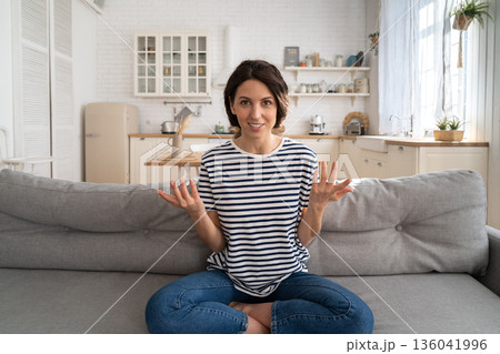 Smiling woman vlogger influencer recording new content to vlog, looking at webcam, sitting on couch. 136041996