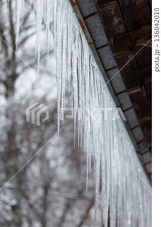 Sharp icicles, ice stalactite hanging from eaves of roof 136042010