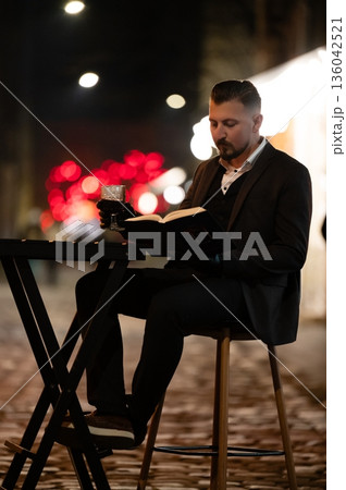 Evening moments of reflection by the cozy streetside table with a captivating book and a warm drink amidst soft city lights 136042521