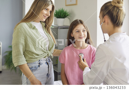Mother and pediatrician with stethoscope during child checkup in clinic room 136043233