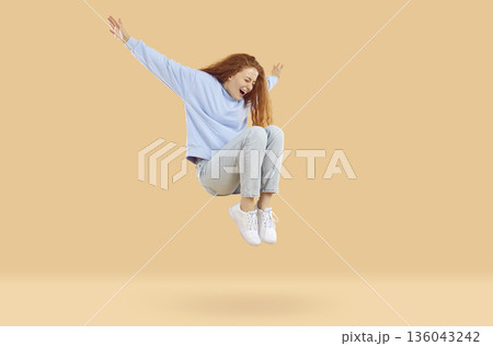 Happy excited teenage girl is happy jumping high and levitating on beige background in studio. 136043242