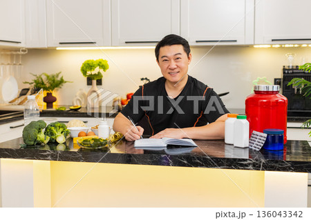 Asian man writes workout plan and records diet in journal with protein powder pills and vegetables Asian man writes workout plan and records diet in journal with protein powder pills and vegetables 136043342
