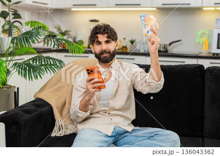 Indian man counting euro money cash salary using smartphone calculator for vacation budget future 136043362