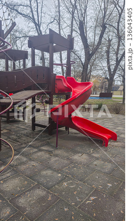 Empty swings on a playground in winter. Park attractions, wooden benches, slides Empty swings on a playground in winter. Park attractions, wooden benches, slides 136043405