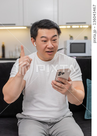Asian man studies online course on smartphone in headphones finds solution shows ok sign sets goal Asian man studies online course on smartphone in headphones finds solution shows ok sign sets goal 136043467
