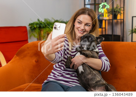 Middle-aged woman with dog makes funny selfies on smartphone laughs and joins video call conference 136043489