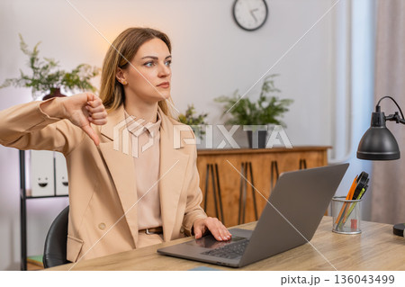 Businesswoman shows thumbs down at laptop dislike gesture unhappy face reacts to bad result review Businesswoman shows thumbs down at laptop dislike gesture unhappy face reacts to bad result review 136043499