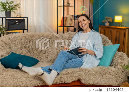 Young woman on sofa carefully writing notes in notebook thoughtfully making important todo list 136044054
