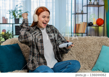 Young woman on sofa playing video game with joystick emotionally reacting to action on screen 136044062
