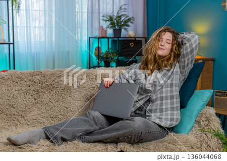 Young woman on sofa yawning stretching closing laptop after long work feeling happy and satisfied Young woman on sofa yawning stretching closing laptop after long work feeling happy and satisfied 136044068