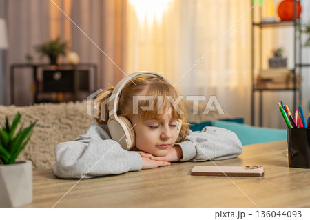 Young girl listening to audiobook with headphones, excitedly reacting to story with open eyes, smile 136044093