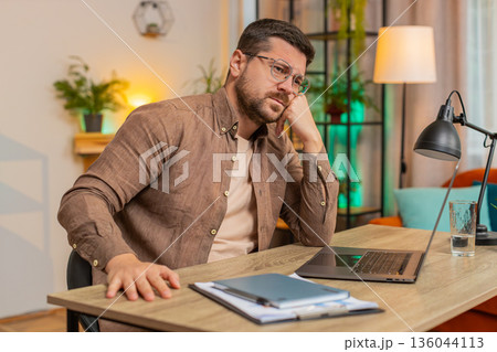 Sad Caucasian young man freelancer looks pensive thinks over life concerns sitting at desk at home 136044113