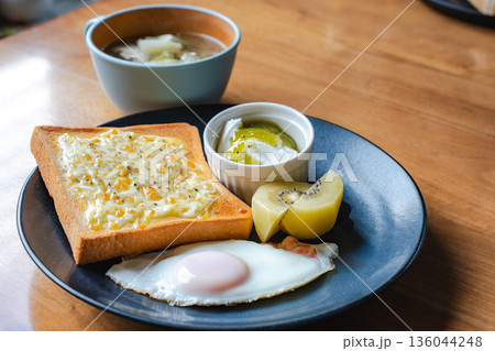 トーストと目玉焼きとスープの朝食セットを木目テーブルに並べる 136044248