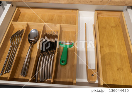 Silverware is neatly placed in a wooden kitchen drawer, with sections for forks, spoons, knives, and a vegetable peeler Silverware is neatly placed in a wooden kitchen drawer, with sections for forks, spoons, knives, and a vegetable peeler 136044430