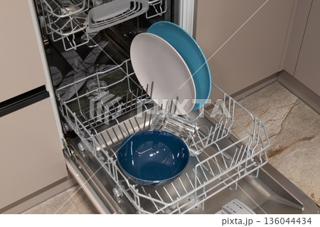 Dishes are organized inside a dishwasher in a kitchen. Plates, bowls, and glasses are visible and ready for a cleaning cycle 136044434