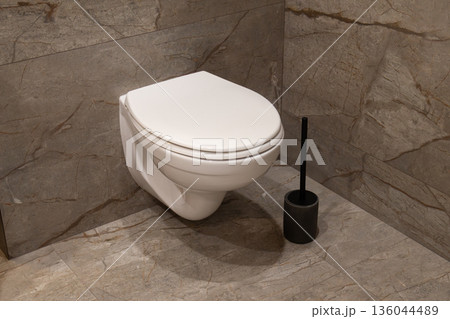 A sleek white toilet is mounted against textured gray marble walls, reflecting modern design trends in bathroom decor A sleek white toilet is mounted against textured gray marble walls, reflecting modern design trends in bathroom decor 136044489