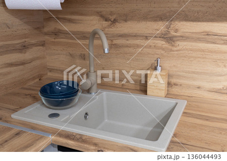 Fresh kitchen scene showcases a sleek sink with a stylish faucet, complemented by a deep bowl and a natural wooden backdrop, embodying simplicity Fresh kitchen scene showcases a sleek sink with a stylish faucet, complemented by a deep bowl and a natural wooden backdrop, embodying simplicity 136044493