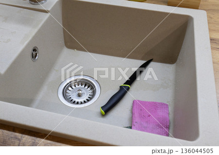A sharp knife lies on the edge of a clean sink next to a cloth, indicating recent meal preparation in a cozy kitchen 136044505
