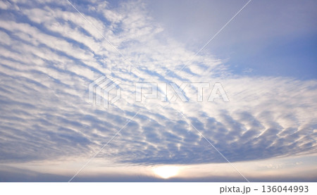 Bright blue sky with gentle clouds and rising sun over a calm horizon 136044993