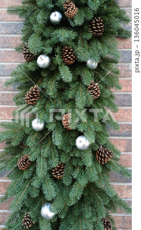 Evergreen garland with pinecone accents and silver balls on brick wall for festive decor Evergreen garland with pinecone accents and silver balls on brick wall for festive decor 136045016