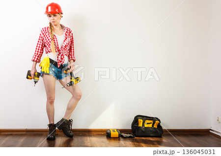 Woman wearing helmet, toolbelt about to drill wall 136045031