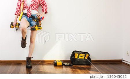Woman wearing helmet, toolbelt about to drill wall Woman wearing helmet, toolbelt about to drill wall 136045032