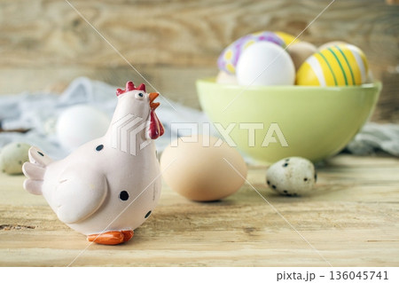 Easter chicken figurine with decorated and natural eggs on wooden background. Rustic still life with fresh farm eggs and decorative chicken figurine. Easter chicken figurine with decorated and natural eggs on wooden background. Rustic still life with fresh farm eggs and decorative chicken figurine. 136045741