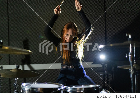 Female musician passionately playing drums in music studio 136047111
