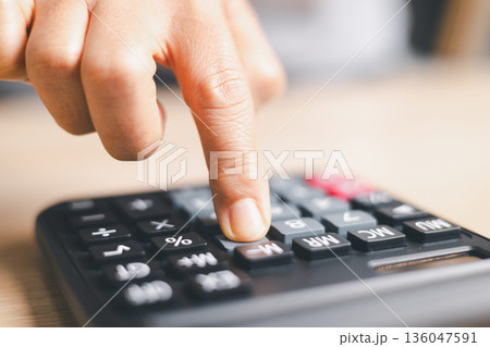 Close-up of a hand pressing calculator keys for budgeting, accounting and financial analysis. Business expense planning, tax calculation, office desk background, copy space for paperwork. Close-up of a hand pressing calculator keys for budgeting, accounting and financial analysis. Business expense planning, tax calculation, office desk background, copy space for paperwork. 136047591
