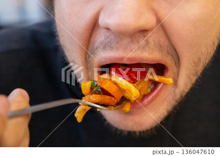 male eating a large forkful of stir fry pasta vegetables with open mouth, showcasing overeating and unhealthy eating habits. concept of obesity, diabetes, gluttony, diabetes, overeating 136047610