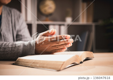 Clasped hands in prayer over an open book, warm light and shallow depth of field, symbolizing faith, devotion, reflection and hope for spiritual guidance during quiet study at home. Clasped hands in prayer over an open book, warm light and shallow depth of field, symbolizing faith, devotion, reflection and hope for spiritual guidance during quiet study at home. 136047618