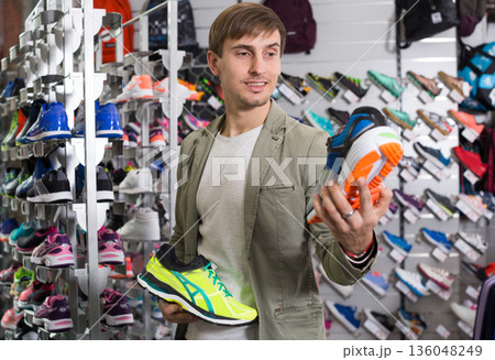 Interested man comparing two pairs of running shoes in store Interested man comparing two pairs of running shoes in store 136048249