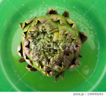 cooked whole artichoke on a green plate cooked whole artichoke on a green plate 136048263