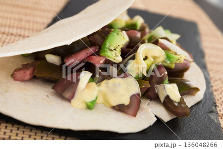 salad of black tomatoes, avocado and onions in Italian tortilla on black stone board 136048266
